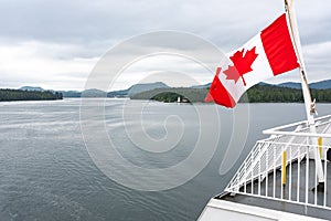 A close up of the Canadian flag flying in the wind at the back of ferry as the boat makes it way through the Inside Passage,