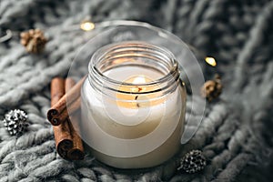 Close-up, candle and cinnamon sticks on the background of a gray knitted element.