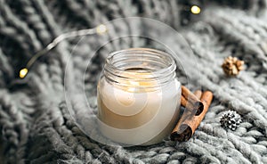 Close-up, candle and cinnamon sticks on the background of a gray knitted element.