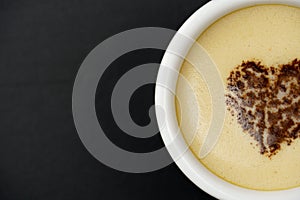 Close-up of cappuccino in the center of the heart, over black background with copy space. Chocolate heart in a mug with a hot