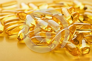 Close up capsules with Vitamin D, E or Omega 3,6,9 fatty acids in bottle top view isolated on yellow. Food supplement oil filled