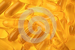 Close up capsules with Vitamin D, E or Omega 3,6,9 fatty acids in bottle top view isolated on yellow. Food supplement oil filled