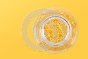 Close up capsules with Vitamin D, E or Omega 3,6,9 fatty acids in bottle top view isolated on yellow. Food supplement oil filled