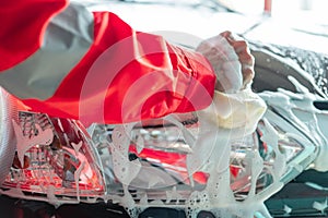 Close up of car cleaner hands in red uniforms cleaning car windows with a foamy sponge