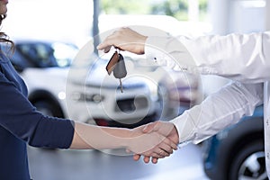 Close-up of car dealer shaking buyer`s hand and giving keys afte