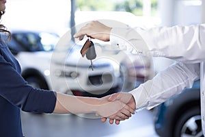Close-up of car dealer shaking buyer`s hand and giving keys afte photo