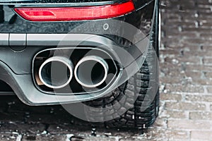 Close up of a car dual exhaust pipe parking lights, brake lights and wheel tires.