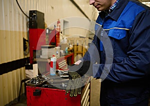 Close-up of a car engineer, mechanic, technician putting on protective work gloves before testing a car in repair shop. Car repair