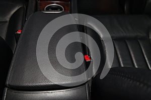 Close-up on the car front armrest with black leather trim, buttons and seat belt in the interior after detailing and dry cleaning