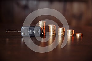 Close-up of car key in front of coins stacked on wooden table. Saving money concept