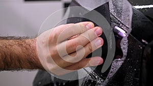 A close-up of a car mechanic applies a protective film to the car body.