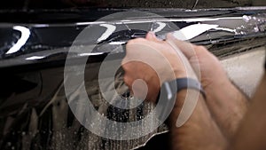 A close-up of a car mechanic applies a protective film to the car body.