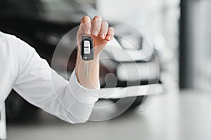 Close up of the car owner's hand holding the delivery key to buyers. Concept of selling cars and giving keys to new