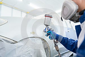 Close up of Car Painter in protective clothes and mask painting automobile bumper with metallic paint and varnish in chamber