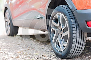 Close up of car tyres. Back view of a parked car over a road covered with autumn leaves.