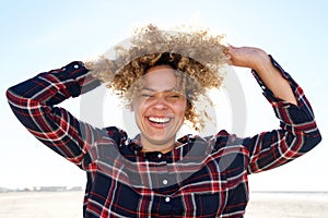 Close up carefree african american woman laughing with hands in hair outdoors