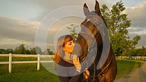 CLOSE UP: Carefree young woman holds her horse's reins while giving it a kiss.