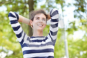 Close up carefree young woman smiling with hands behind head outdoors