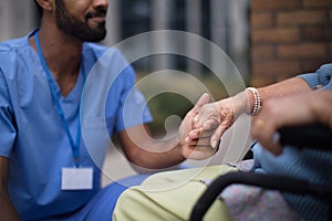 Close-up of caregiver holding hand of his client on wheelchair.