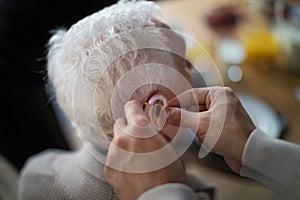 Close-up of caregiver man's hand inserting hearing aid in senior's man ear.