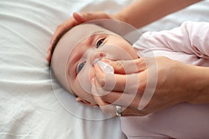 Close up of caring  mother with nasal pump to clean her baby& x27;s nose. Baby lying in bed