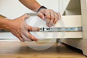 Close up of carpenter hands installing wooden drawer on sliding skids in contemporary cupboard cabinet