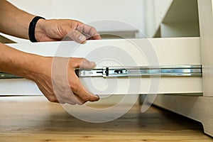 Close up of carpenter hands installing wooden drawer on sliding skids in contemporary cupboard cabinet