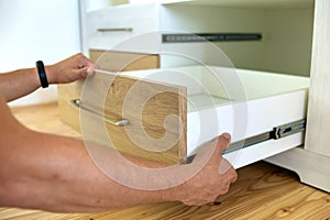 Close up of carpenter hands installing wooden drawer on sliding skids in contemporary cupboard cabinet