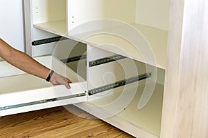 Close up of carpenter hands installing wooden drawer on sliding skids in contemporary cupboard cabinet