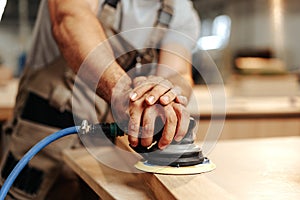 Close up of carpenter hands sanding wood with orbital sander at workshop