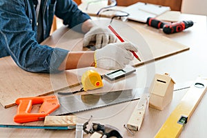 Close-up carpenter hands wearing work gloves draw the cutting line with a pencil on a wooden board. Construction industry,