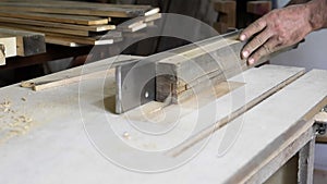 Close-up: a carpenter in his workshop saws a wooden board with a circular saw, makes furniture parts in natural light. A