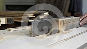 Close-up: a carpenter in his workshop saws a wooden board with a circular saw, makes furniture parts in natural light. A