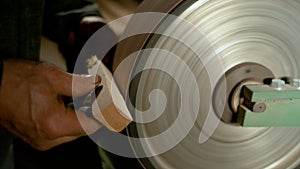 CLOSE UP: Carpenter holds a piece of wood against a wheel covered with sandpaper photo