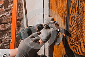 Close-up, the carpenter installs a custom lock in the front metal door, using a drill and hammer and other tools