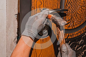 Close-up, the carpenter installs a custom lock in the front metal door, using a drill and hammer and other tools