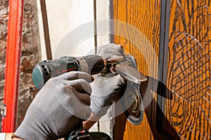 Close-up, the carpenter installs a custom lock in the front metal door, using a drill and hammer and other tools