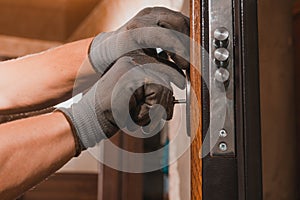 Close-up, the carpenter installs a custom lock in the front metal door, using a drill and hammer and other tools