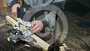 Close-up of a carpenter`s hand working with an manual electric cutter in a home workshop. Finishing wooden parts