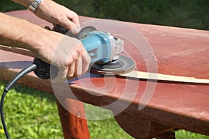 Close-up of carpenter`s hands working with electric sander - polishing old color from wooden table
