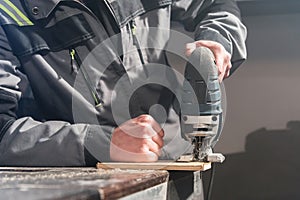 Close up of carpenter`s hands working power tools for processing wood. Power Jigsaw