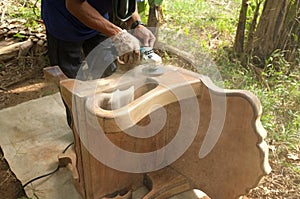 Close up of a carpenter scrubbing wood chair with handheld electric scrubber