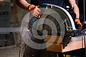 Close-up of carpenter using electric circular saw to cut wood planks