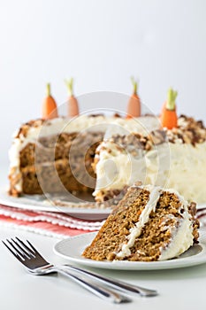 A close up of a carrot cake with cream cheese frosting and a slice of cake in front ready for eating.