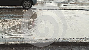 Close-up cars drive along the road with holes and muddy puddles.