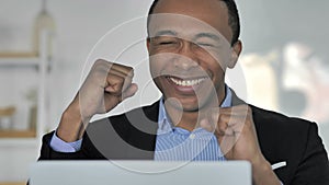 Close up of casual Afro-American businessman celebrating success, working on laptop