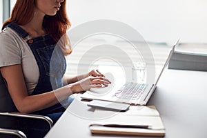 Close Up Of Casually Dressed Young Businesswoman Working On Laptop At Desk In Modern Workplace