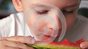 Close-up of a Caucasian boy 6-8 years old eating a red juicy watermelon, the juice flows down the lips of the child. Selective foc