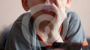 Close-up of a caucasian boy lying down watching TV holds a remote control in his hand. The child is resting while watching tv prog