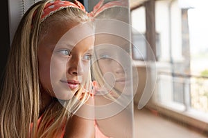 Close-up of caucasian elementary schoolgirl leaning on glass window in classroom